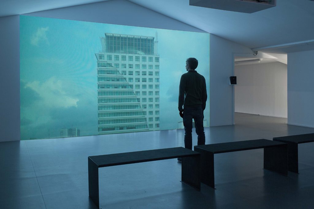 Personnage debout face à un écran représentant un gratte-ciel inquiétant