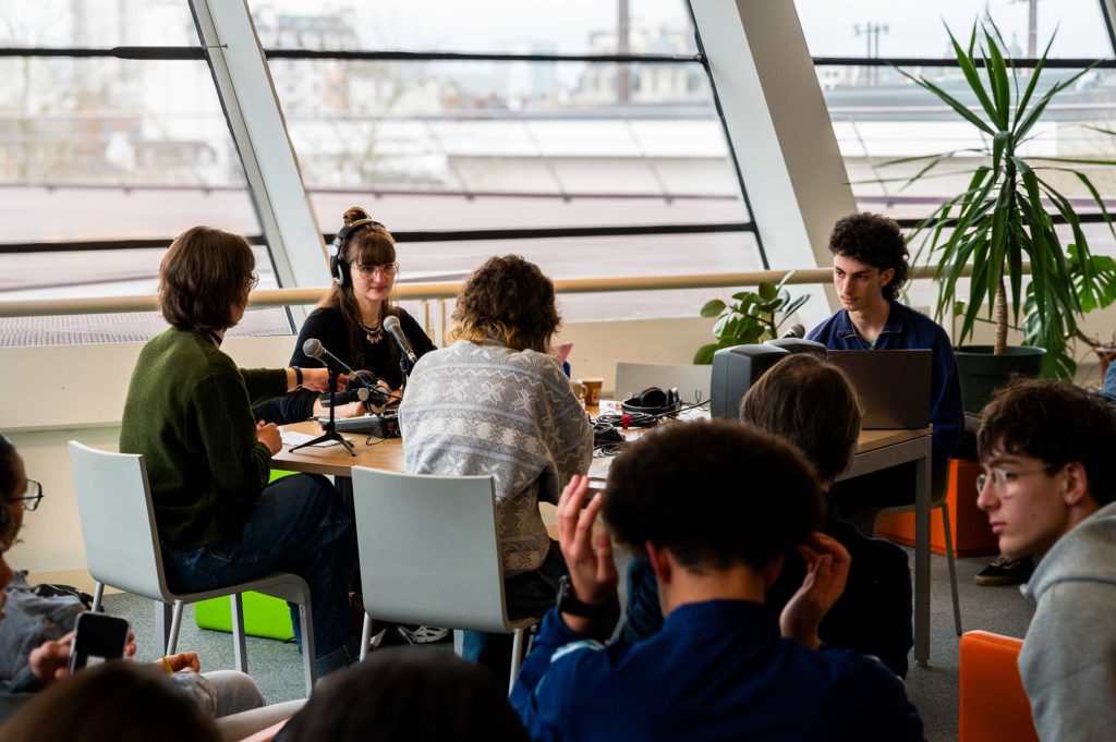 Des jeunes gens assis autour d'un plateau radio. Baie vitrée en fond.
