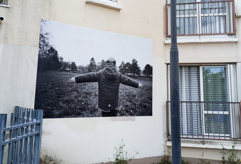 Une photo noir et blanc d'un enfant de dos, les bras écartés. La photo est collée sur le mur d'un immeuble.