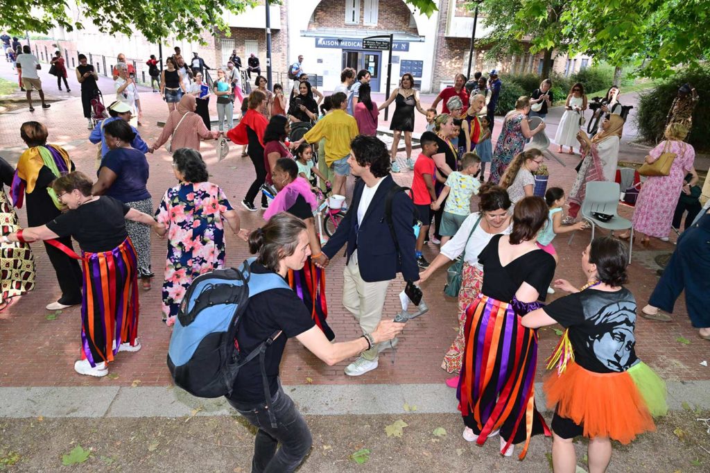 Des habitants dansent sur une place. Une ronde s'est formée.