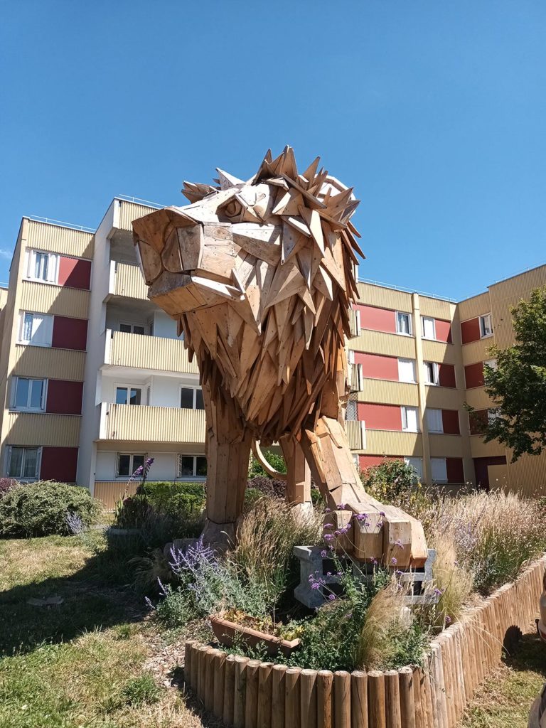 Un statue de lion fabriquée en bois, en pied d'immeuble.